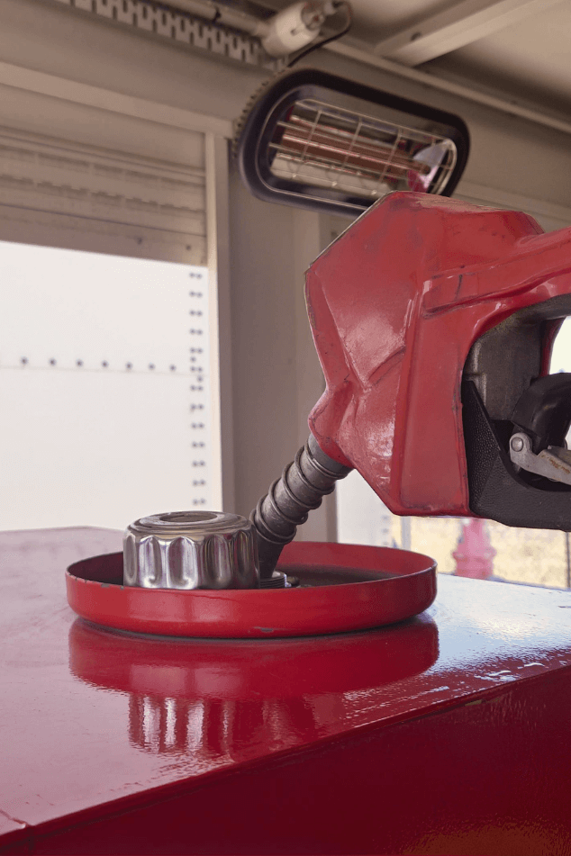 Red diesel fuel nozzle inserted into the opening of a metal fuel tank indoors